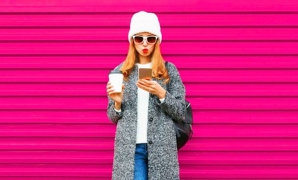 Cool hipster girl using phone holding coffee cup on colorful pink wall background - Fotografie, Obrázek