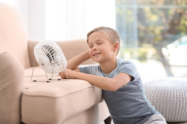 Little boy relaxing in front of fan at home. Summer heat - Foto, afbeelding