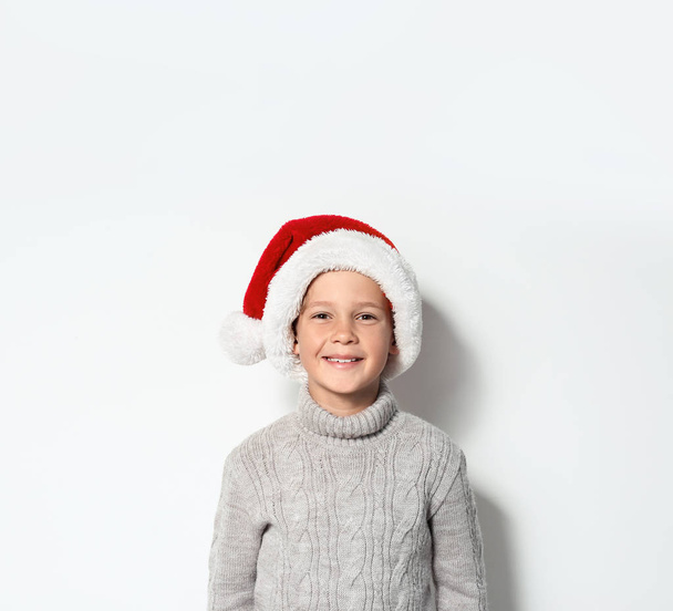 Cute little boy in warm sweater and Christmas hat on white background - Foto, afbeelding
