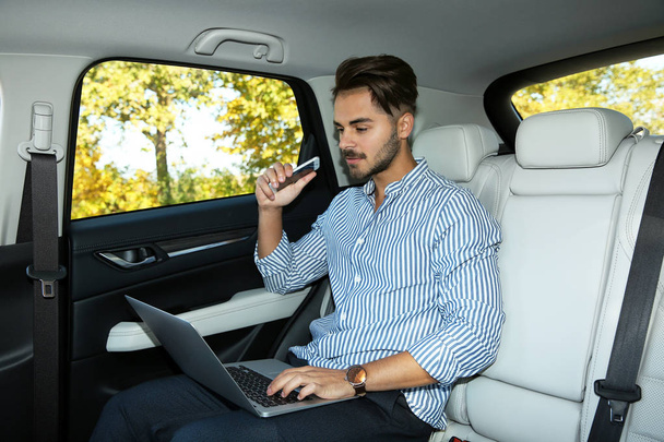 Fiatal jóképű férfi telefon használ laptop, a hátsó ülésen az autó - Fotó, kép