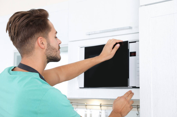 Young man using modern microwave oven at home - Fotoğraf, Görsel