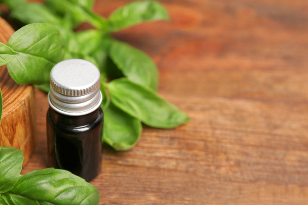 Glass bottle of basil oil with leaves and space for text on wooden table - Photo, Image
