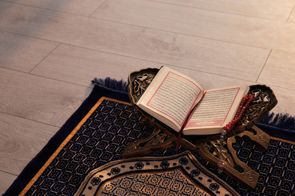 Rehal with open Quran and Muslim prayer beads on rug indoors. Space for text - Foto, Bild