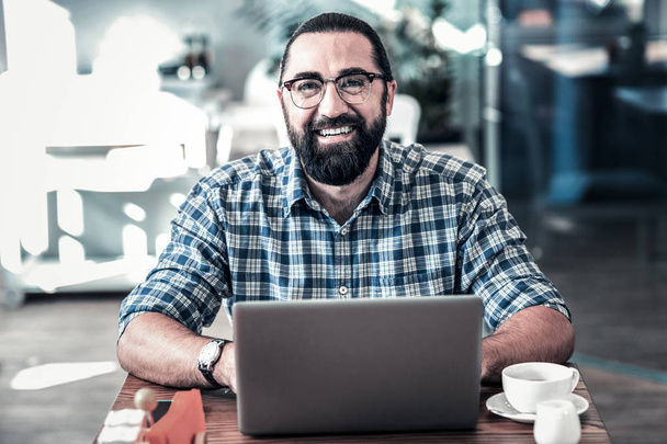 Smiling pleasant businessman feeling joyful working on laptop - Photo, image
