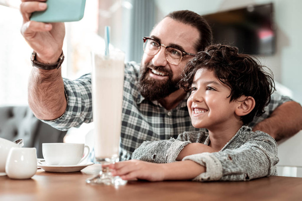 Happy father holding blue smartphone making selfie with son - Foto, Imagen