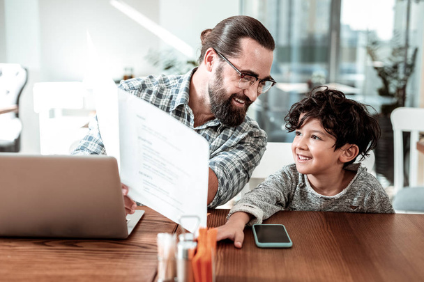Cute dark-eyed son looking at the menu coming to restaurant with father - Photo, Image
