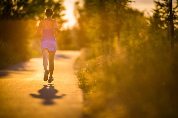 Young woman running outdoors on a lovely sunny summer evening (shallow DOF; color toned image) - Photo, Image
