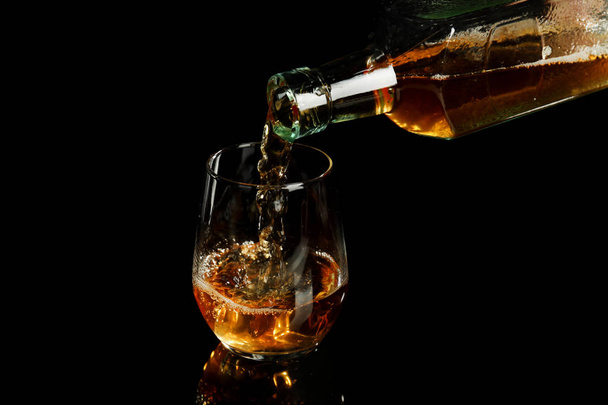 Pouring of whiskey from bottle into glass on black background - Photo, Image