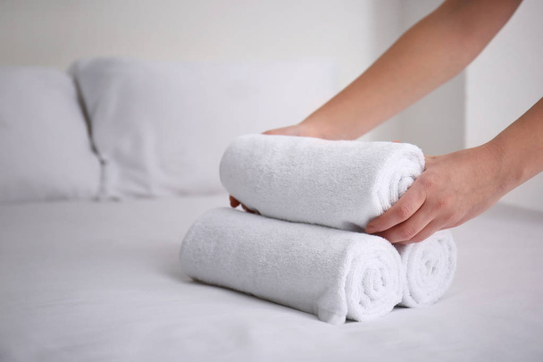 Woman putting clean white towels on bed indoors - Photo, Image