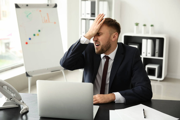 Emotionele jonge zakenman na fout maken tijdens het werken met de laptop in kantoor - Foto, afbeelding