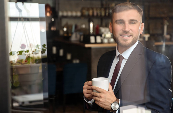 Knappe zakenman koffie drinken in café, weergave via venster ten opzichte van buiten - Foto, afbeelding