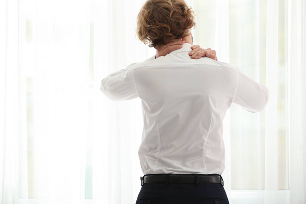 Junger Geschäftsmann leidet unter Nackenschmerzen am Fenster - Foto, Bild