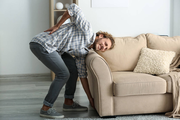 Young man suffering from back pain after carrying heavy furniture - Foto, Imagen
