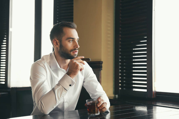 Young man with glass of whiskey and cigar in pub - Foto, afbeelding