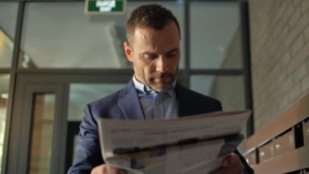 Caucasian 30s man in elegant suit wear reading the morning newspaper standing near with post boxes in business centre. Success confident modern human keep in hands corporate magazine, urban lifestyle - Footage, Video