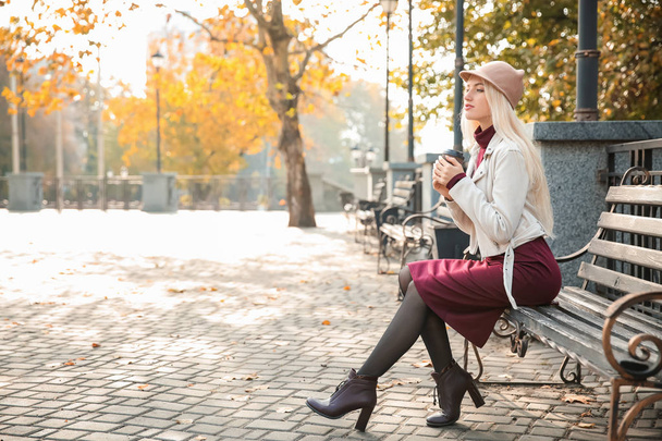秋の公園でベンチに座って美しいファッショナブルな女性 - 写真・画像