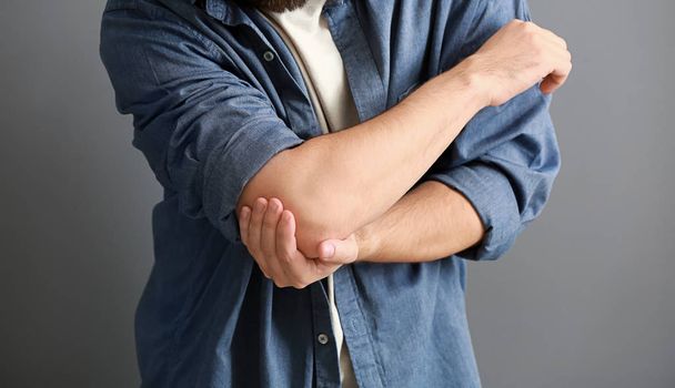 Ο άνθρωπος που πάσχουν από τον πόνο στον αγκώνα σε γκρι φόντο, κοντινό πλάνο - Φωτογραφία, εικόνα