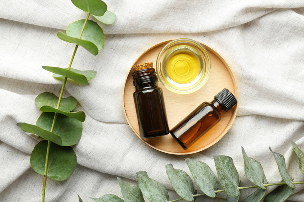 Tigela e garrafas de óleo essencial de eucalipto sobre pano claro
 - Foto, Imagem