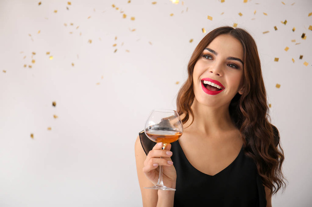Beautiful young woman with glass of wine and falling confetti on light background - Photo, Image