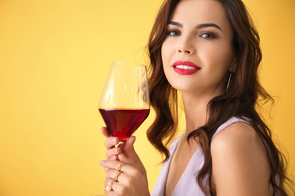 Beautiful young woman with glass of wine on color background - 写真・画像