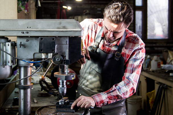 Portrait of blacksmith in leather apron drills workpiece - Fotografie, Obrázek