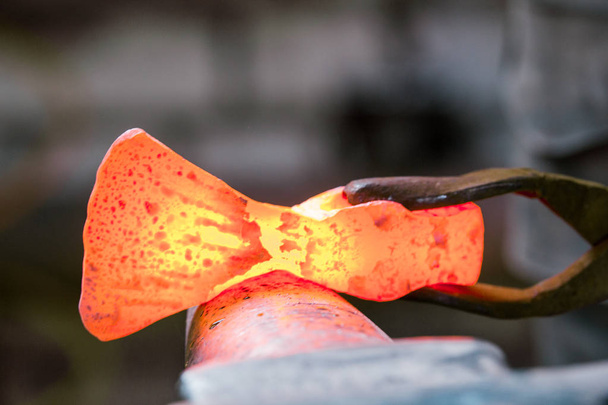 Blacksmith työskentelee punaisen kuuman metallin työkappaleen uuden kirveen kanssa alasin päällä. Keskity metalliin
 - Valokuva, kuva