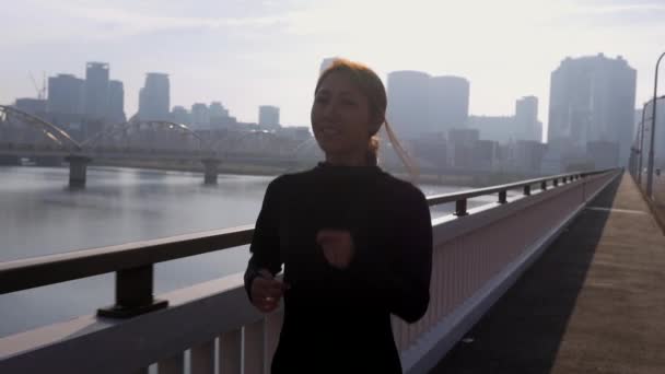 Japanese fitness model running across bridge, city skyline behind, HD, slow motion. - Filmati, video
