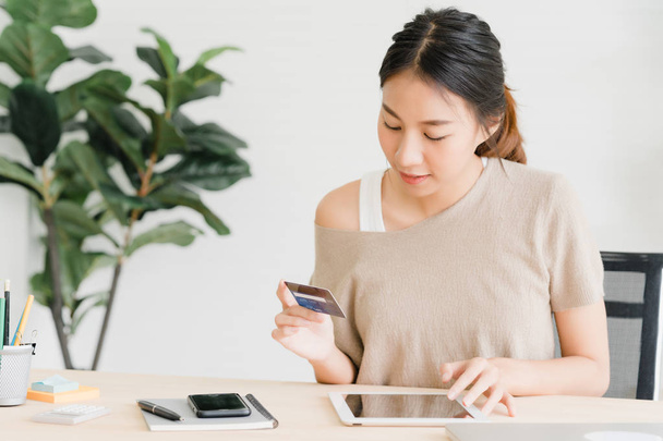 Mulher asiática bonita usando smartphone comprando compras on-line por cartão de crédito, enquanto usar suéter sentado na mesa na sala de estar em casa. Mulher de estilo de vida em casa conceito
. - Foto, Imagem