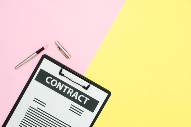 Diseño plano de escritorio de oficina - Vista superior de un documento de contrato y un bolígrafo en color pastel rosa y amarillo con espacio de copia. Fondo de espacio de trabajo de pantalla a color pastel
. - Foto, imagen