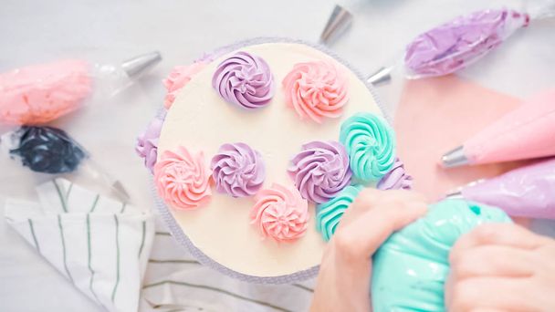 Deitado. Piping rosetas de creme de manteiga cor pastel em um bolo branco para fazer um bolo de unicórnio
. - Foto, Imagem