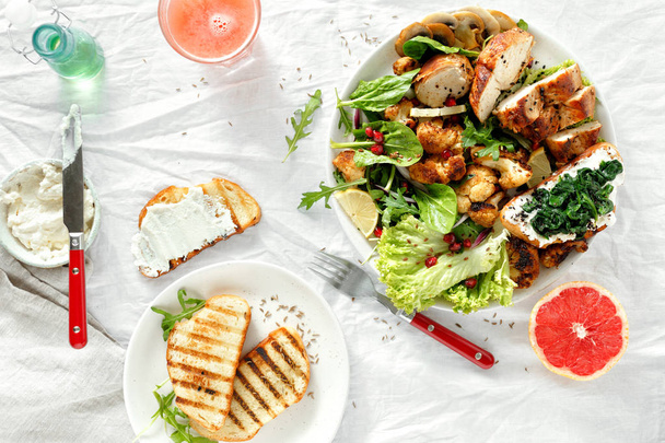Lunch food bowl of fresh salad with hicken steak and fried cauliflower on white background with grapefruit fresh and toasts top view. Healthy food concept - Photo, image