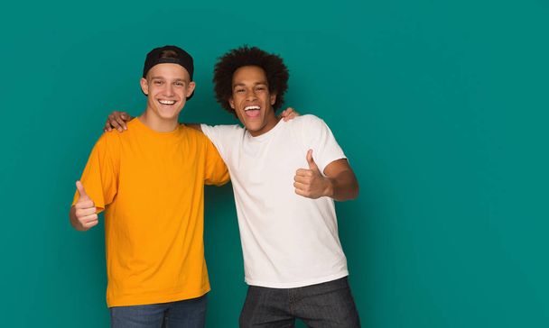 Teenage friends showing thumbs up over blue background - Foto, Bild