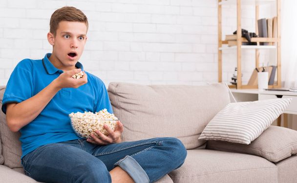Adolescente impresionado viendo películas y comiendo palomitas de maíz
 - Foto, Imagen