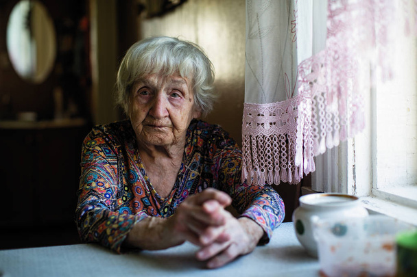 Portrait of an elderly woman sitting in the kitchen. - Фото, зображення
