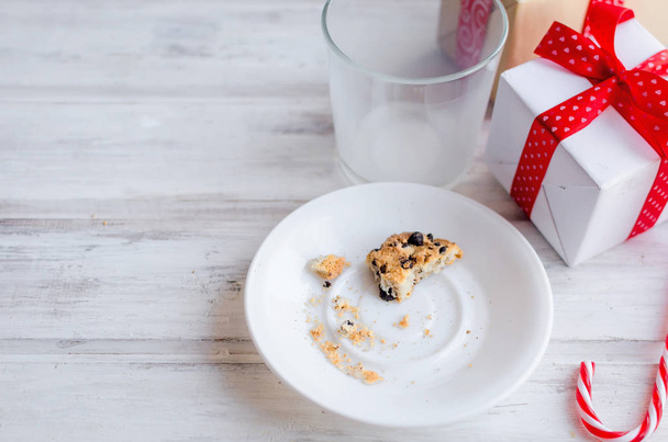 An empty glass of milk with candy and cookies with chocolate chip for Santa on christmas eve on white wooden table. Christmas card. - Photo, image
