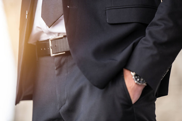 крупним планом смарт бізнесмен рука в кишені чекає з годинником в красивому чорному костюмі сонце на відкритому повітрі
 - Фото, зображення