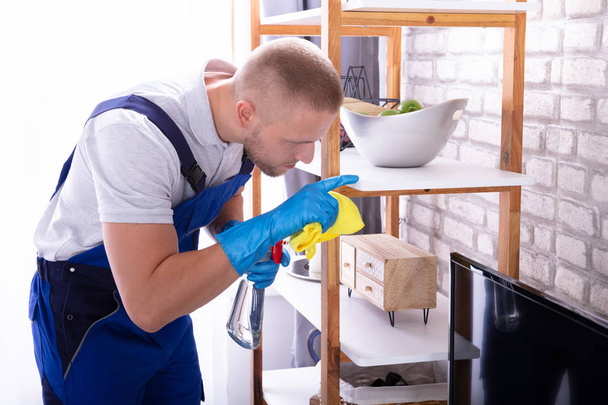 Side View Of A Young Male Janitor Cleaning Shelf In House - Foto, imagen