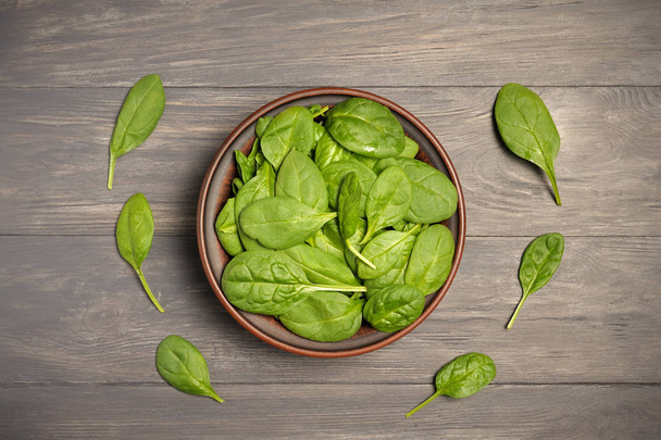 Groene spinazie bladeren in bruin kom op donkere groene voedsel achtergrond als een gezond eten concept van verse tuin produceren biologisch geteelde als een symbool van gezondheid. Biologisch voedsel. Top View.Copy ruimte - Foto, afbeelding