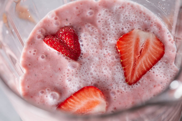 Closeup of milk drink with healthy strawberry slices in a blender. Home-made berry shake. Top view - Фото, зображення
