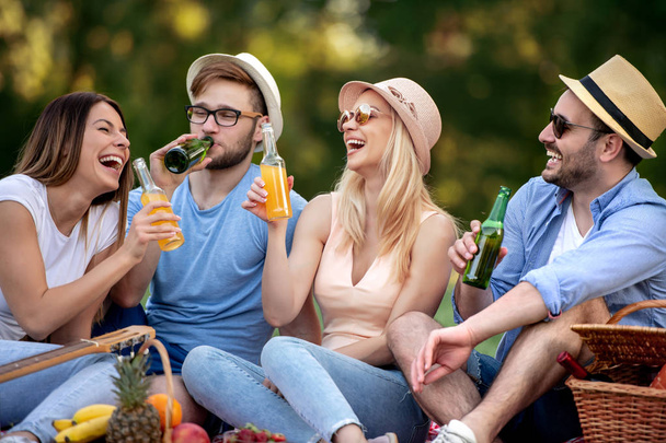 Grupa młodych przyjaciół ciesząc się czas na piknik, napój w pięknej przyrody. - Zdjęcie, obraz