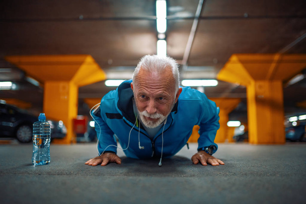 Portret van senior atletische man doet push ups buitenshuis. - Foto, afbeelding