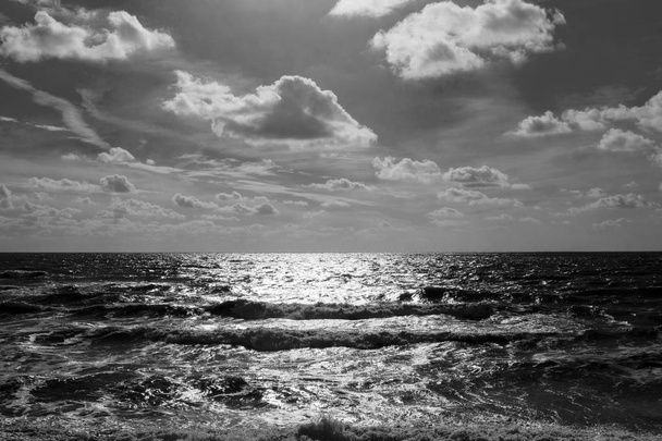 Mer et ciel dans la moitié inférieure est une mer calme, à l'horizon est une ligne de lumière brillante chatoyante blanche, dans la moitié supérieure est le ciel couvert de nuages pelucheux, photographie noir et blanc
  - Photo, image