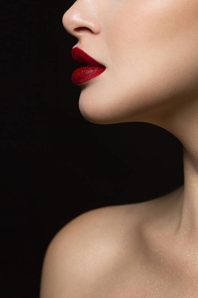 Close-up of the lower part of the face of a woman with perfect skin and plump, expressive lips the color of wine. An image on an isolated black background adds glamor to the image. - Foto, Bild