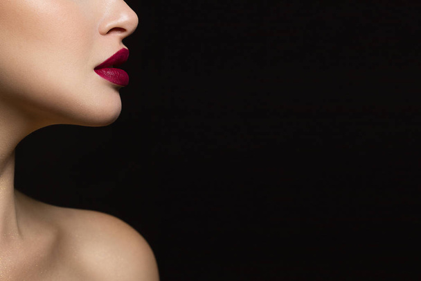 Close-up of the lower part of the face of a woman with perfect skin and plump marsala-colored lips. An image on an isolated black background adds glamor to the image. - Фото, изображение