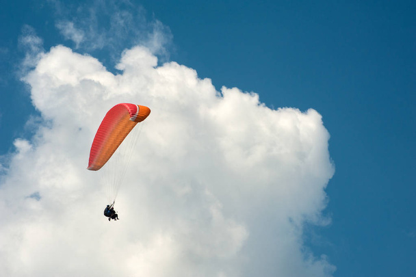 Yksin varjoliito lentää sinisellä taivaalla taustalla pilviä. Laskuvarjohyppy taivaalla aurinkoisena päivänä
. - Valokuva, kuva