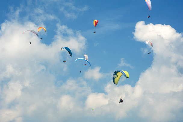  Laskuvarjohyppy sinisellä aurinkoisella taivaalla. Ryhmä varjoliittolaisia lentää kesäisin aurinkoisena päivänä karpaateilla. Laskuvarjohyppääjät pilvien taustalla
. - Valokuva, kuva