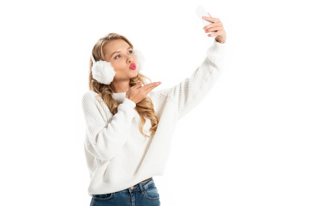 happy blonde girl blowing kiss while taking selfie on smartphone isolated on white - Foto, Imagen
