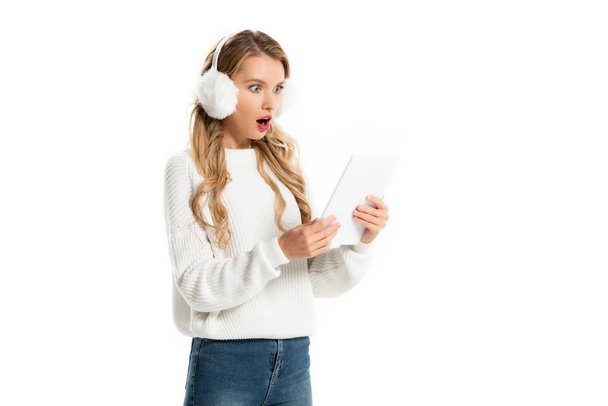 shocked blonde girl in stylish earmuffs looking at digital tablet isolated on white  - Foto, afbeelding