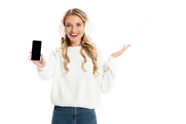 excited girl in earmuffs showing smartphone with blank screen isolated on white - Zdjęcie, obraz