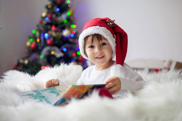 Cute adorable boy reading a book in front of the christmas tree, christmas time - Foto, Bild